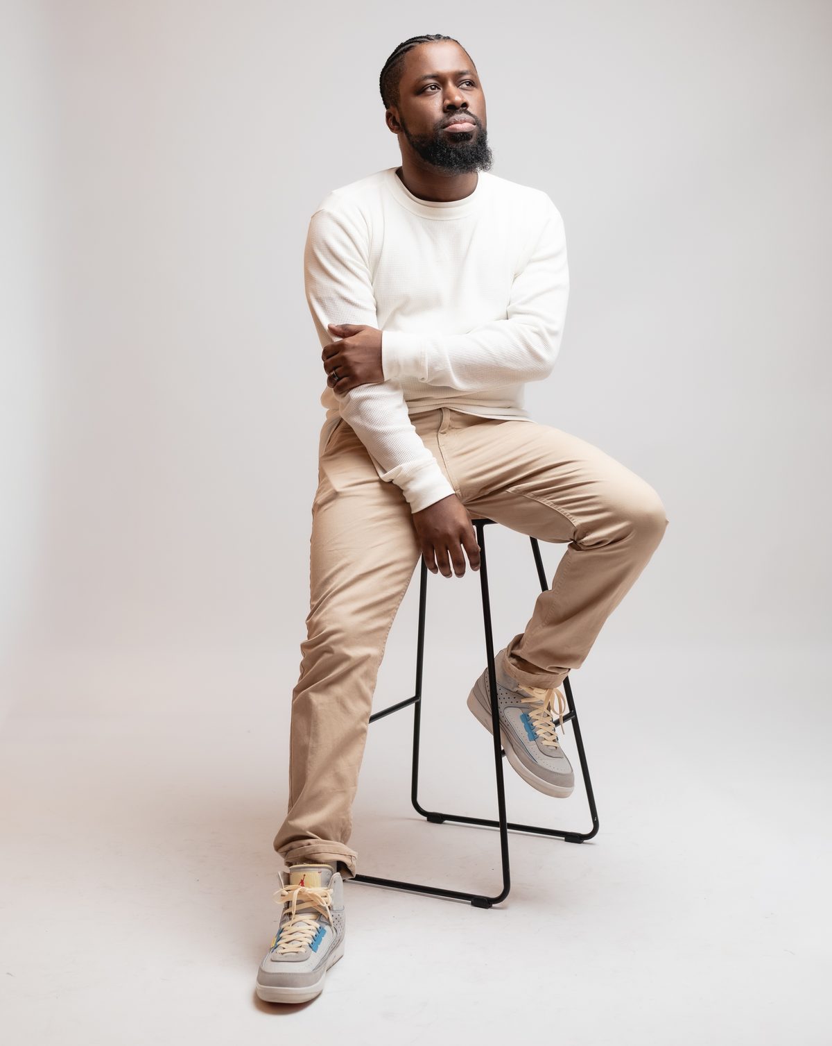 Portrait of Romel Sylne Jr. seated on a stool, arms crossed